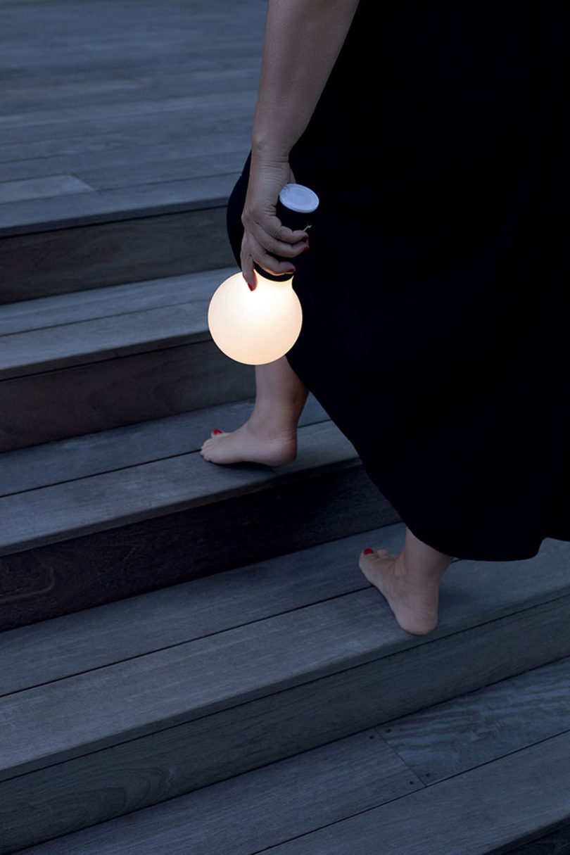 a light-skinned person wearing black carries an outdoor light shaped like a lightbulb up stairs