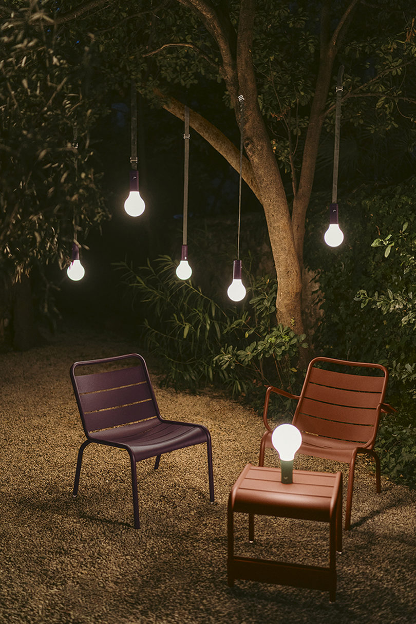 outdoor bulb lighting hangs from a tree over two outdoor chairs