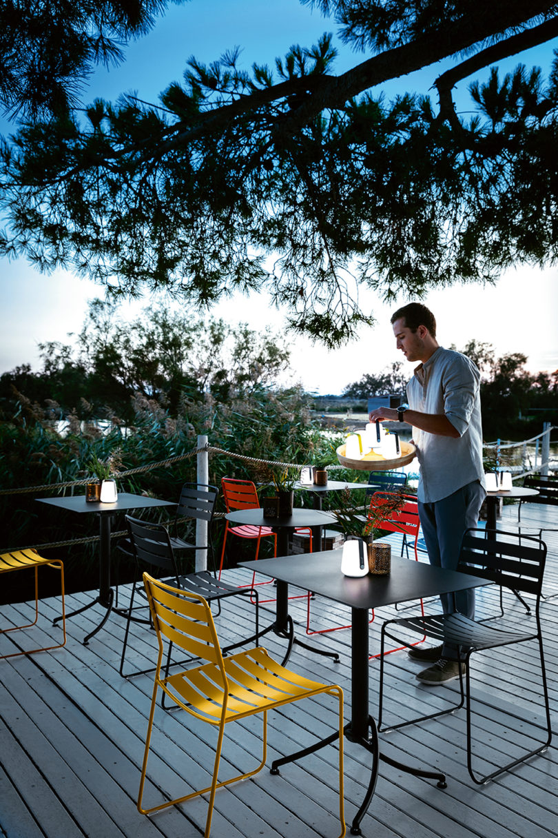 a light-skinned man setting LED lanterns on colorful outdoor dining tables