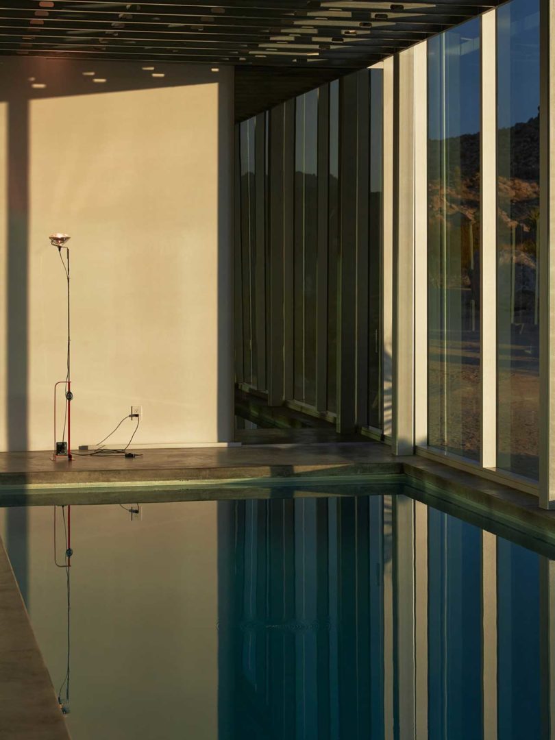 interior shot of dimly lit modern house with single floor lamp at far end in front of pool