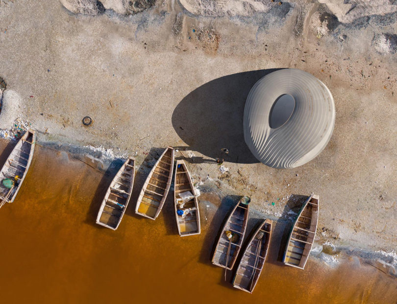 Overhead view of Hassell 3D printed Climate Responsive Pavilion set along shoreline with small wooden boats nearby.
