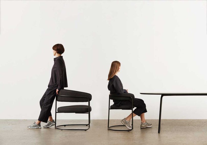 two women wearing all back post with two curved arm chairs