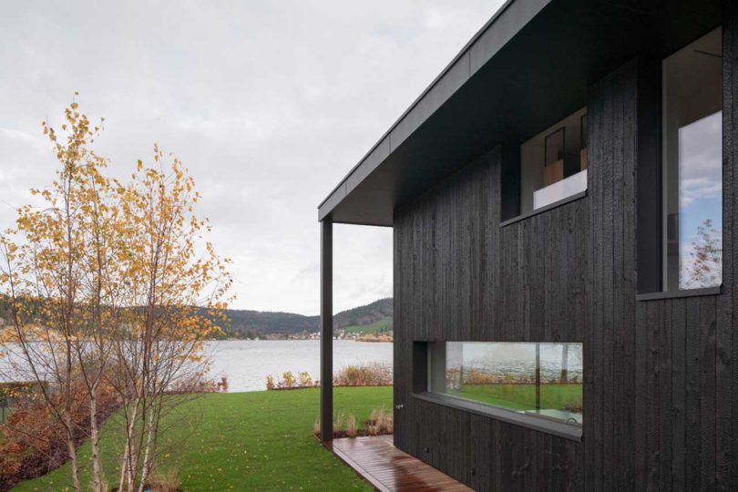 angled side view of exterior of modern black house looking at lake