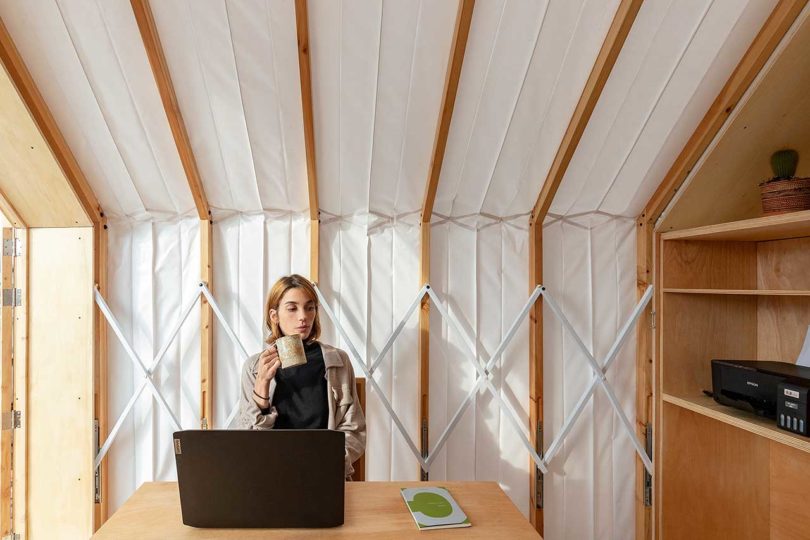 view inside expandable living shelter looking to side with woman sitting at table with laptop