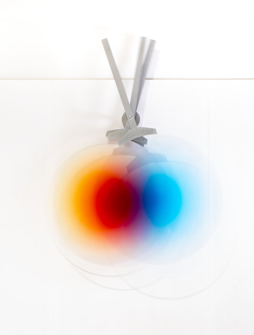 three pendulums in different colors swing to create different hues when they overlay one another