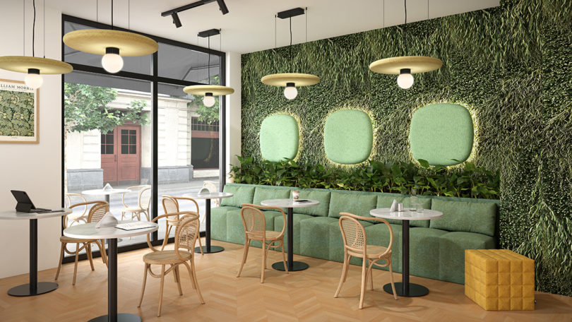 Cafe setting with three lime hued BuzziPebl sconces on wall and five round light yellow BuzziSurf pendant lights overhead with a faux grass lined wall in the background.