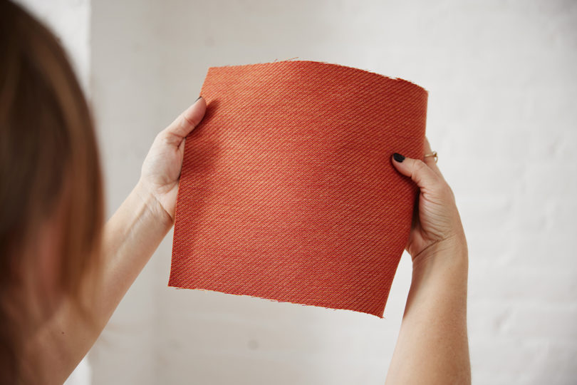 two hands holding up a coral colored fabric swatch