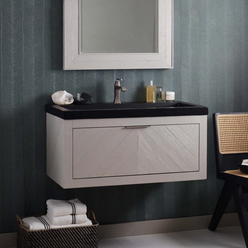 A black sink sits on a grey wall-mounted cabinet under a rectangular mirror with a matching frame