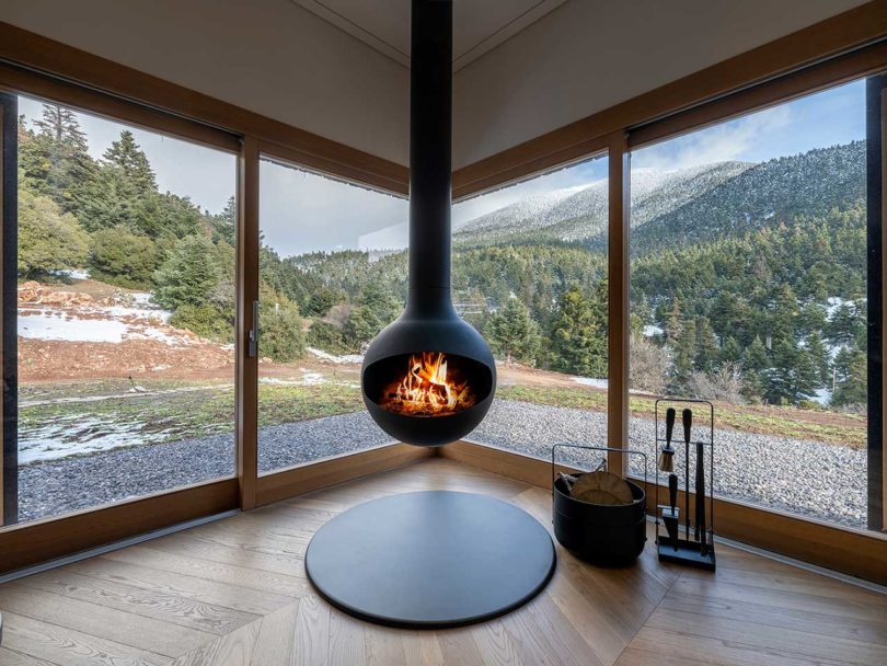 interior view of corner of modern living room with hanging fireplace looking out windows to mountains