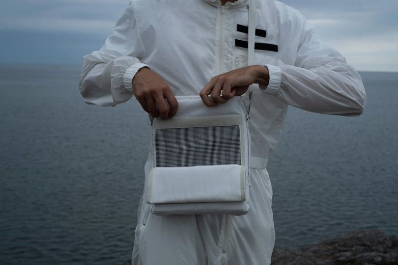 Crop torso of someone in all-white reaching into open Teenage Engineering OB–4 SHOULDER BAG in remote cold outdoor setting.
