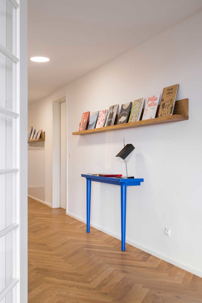 angled view of apartment entry with bright blue console table with wall mounted wood shelf above