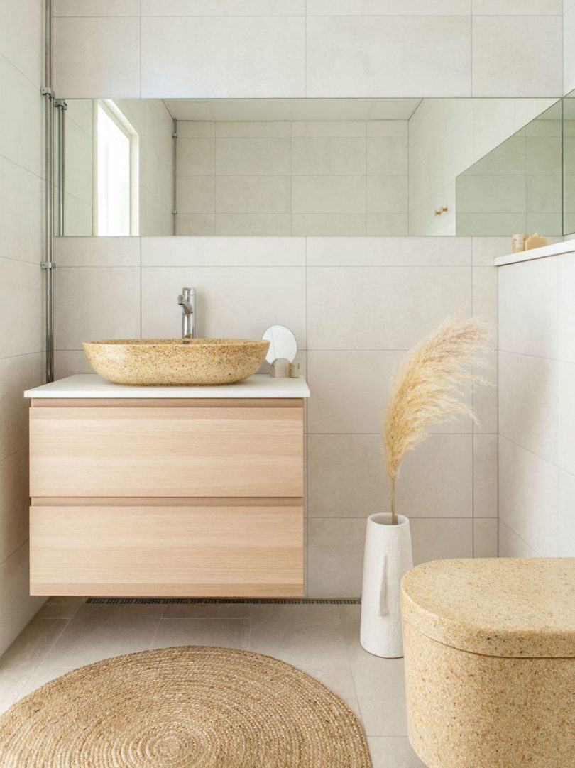 Neutral natural hue bathroom with freestanding one on-top counter basin sink with round mirror to the left and Block toilet on the right.