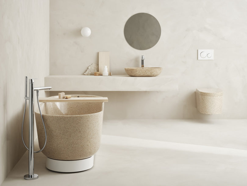 Neutral natural hue bathroom with freestanding Woodio tub on the left, one on-top counter basin sink with round mirro in middle and Block toilet on the right.