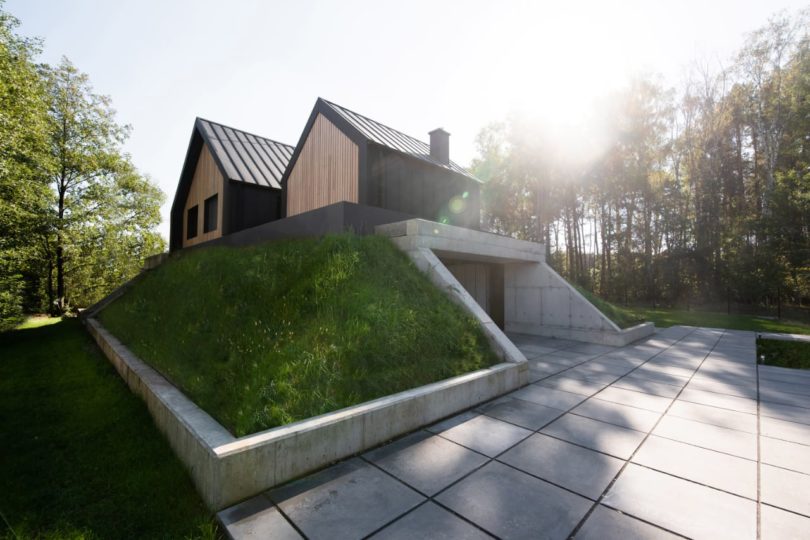 corner exterior view of modern black house with grassy hill hiding a concrete garage