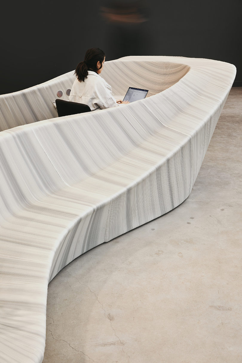 woman sitting at sculptural, white and grey furniture in office lobby