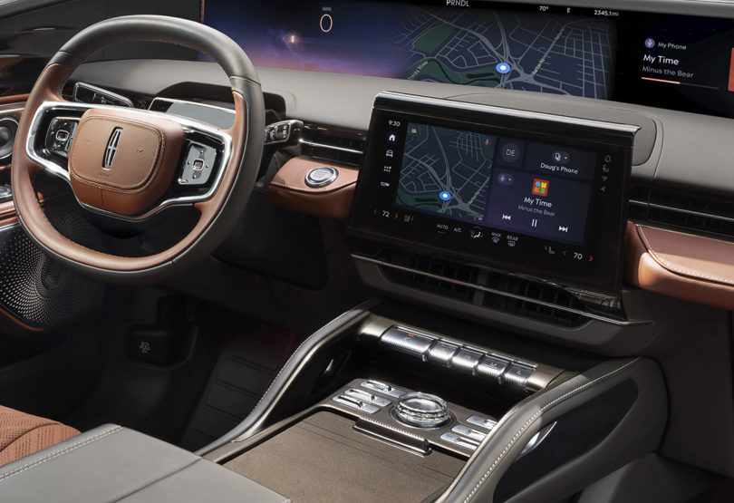 Wide angle shot of 2024 Lincoln Black Label Nautilus Hybrid with Redwood interior trim showing 48-inch horizontal display and 11-inch touchscreen control in center with crystal trim knob.