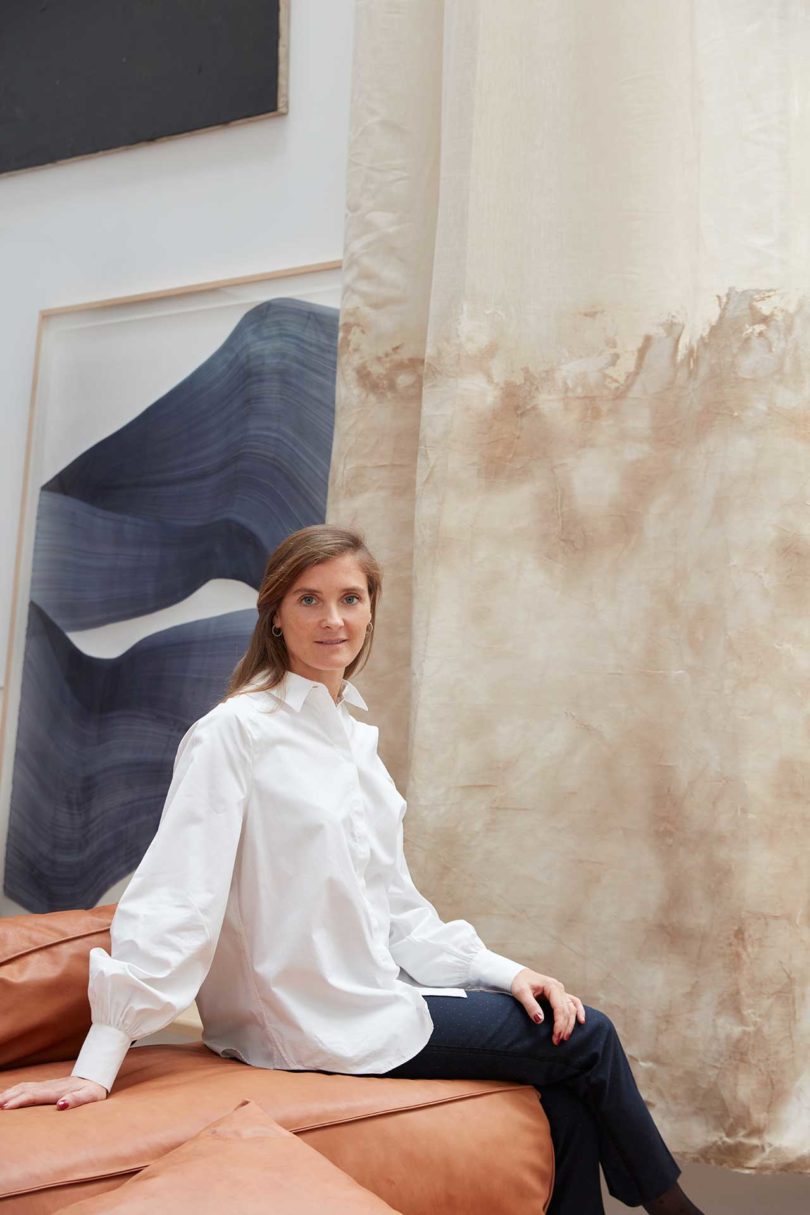 gallerist Amélie du Chalard sitting sideways in front of art