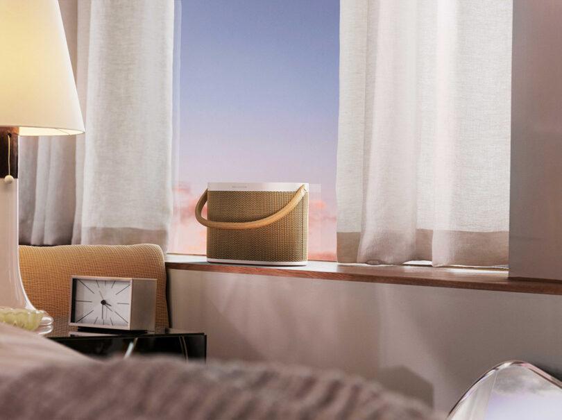 3D render of the A5 speaker in an imaginary modern bedroom with gradient light outside and bedside lamp and clock nearby.