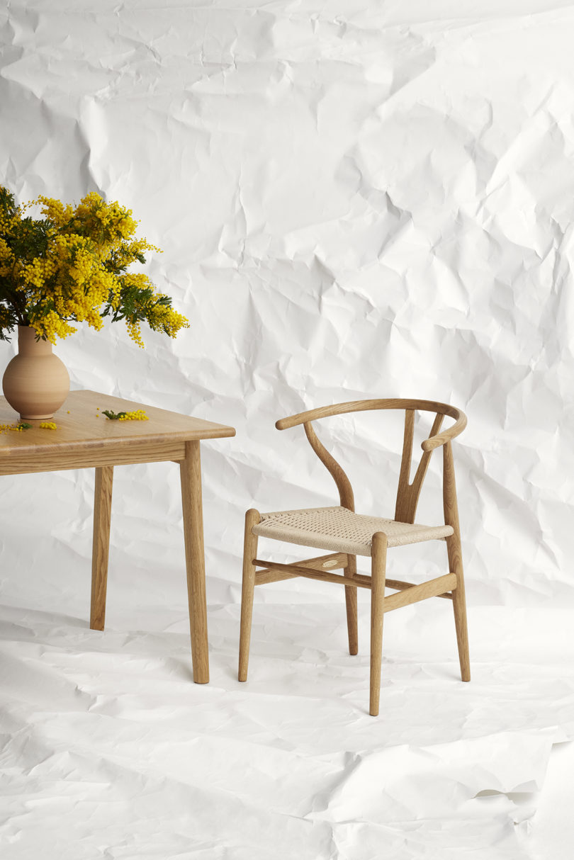 wishbone chair in oak next to a dining table with a vase of yellow flowers