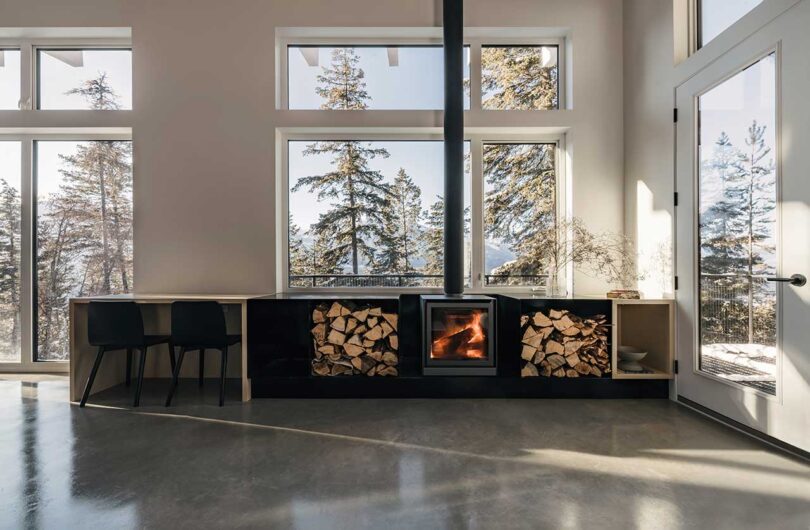 interior view of modern living space with fireplace and cabinets of wood with large windows looking out to snowy trees