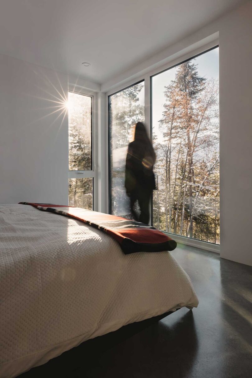 angled corner view of modern bedroom with woman looking out the windows to surrounding trees