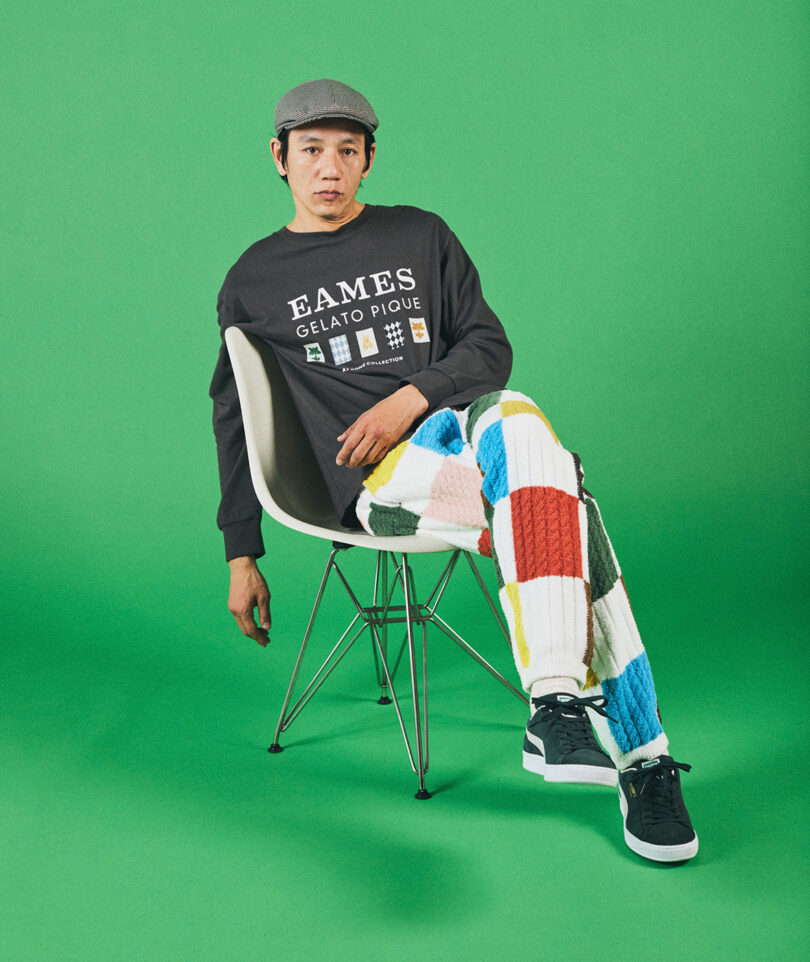 man sitting slouched on a white chair with an eames tshirt on with checkered pants on green background