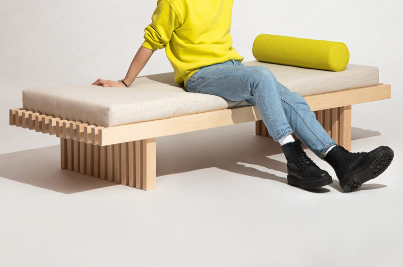 person wearing jeans and a neon yellow sweater sitting on a light wood daybed with light upholstery and neon yellow bolster pillow
