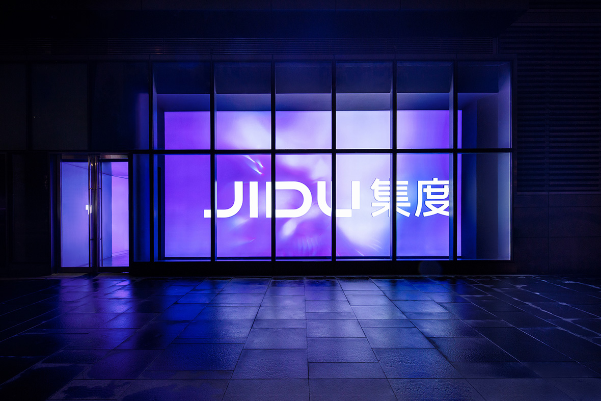 Exterior front of JIDU showroom with large JIDU logo displayed on screens in purple graphics and light.