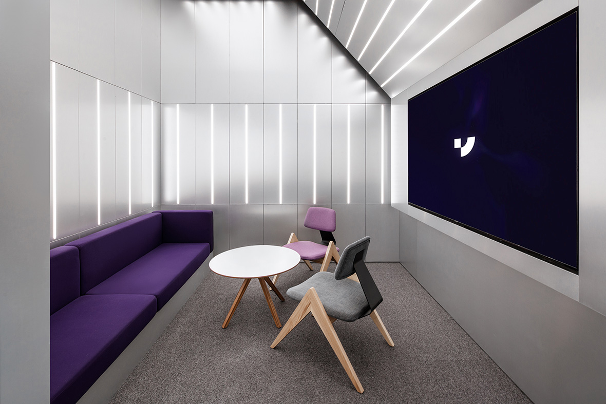 Customer seating area with two seats and one long purple bench with large display to the right and angled ceiling.
