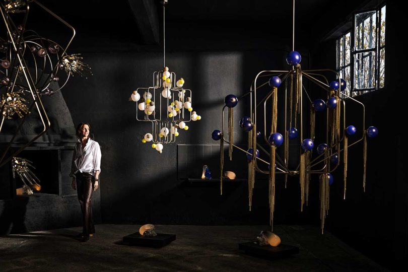 moody dark room with illuminated mobile lights hanging and artist Lindsey Adelman posing