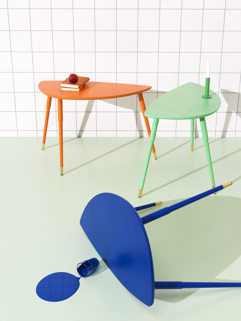 سه میز کناری رنگارنگ IKEA در اتاقی با کاغذ دیواری مشبک سفید با کفپوش سبز روشن.  یک میز به رنگ آبی پر جنب و جوش در کنار آن روی زمین قرار دارد و مایع آبی شبیه‌سازی شده‌ای از یک فنجان بیرون می‌آید.