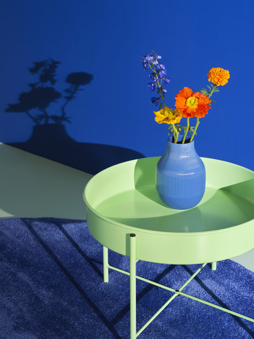 میز کناری سبز ikea در برابر کفپوش آبی تیره با گلدان گل در بالا