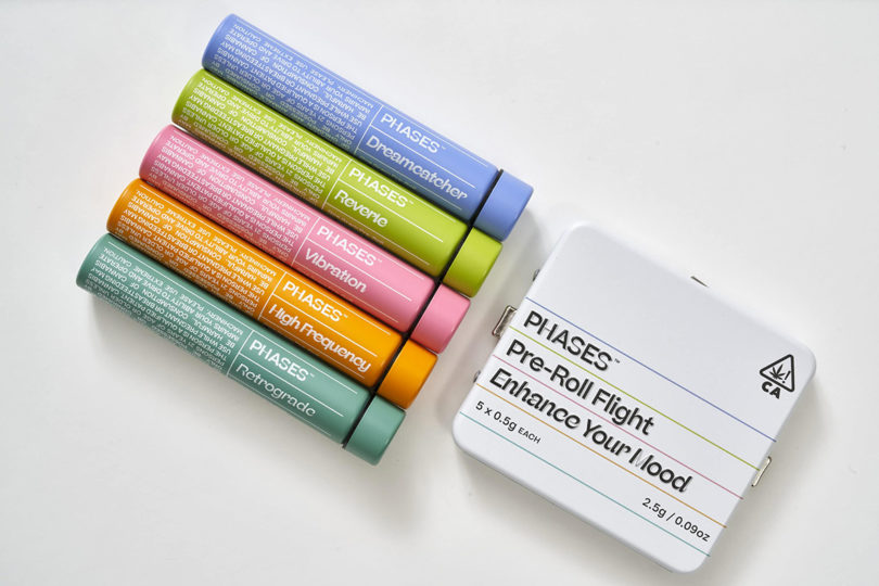 Multi-color tubes of Phases cannabis stir-in pack next to metal tin for brand's pre-rolls.