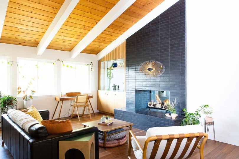 angled interior view of modern living room with angled wood beam ceiling and black tile fire place