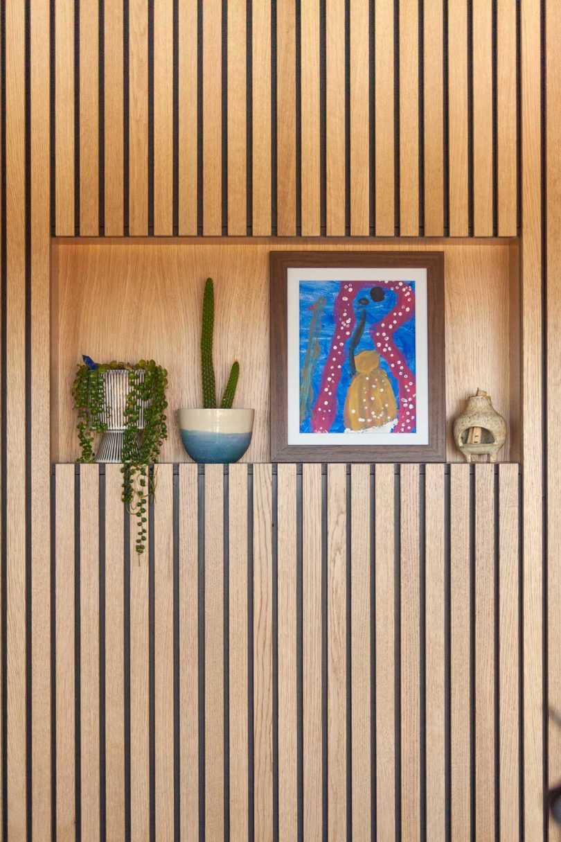 closeup view of embedded shelf in wood paneled wall with plants and artwork