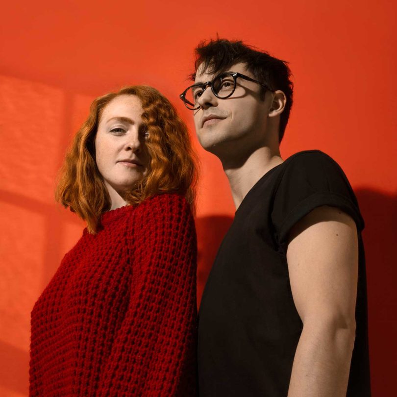 man and woman standing sideways facing camera with red background