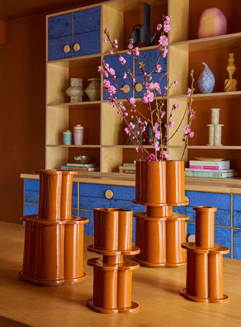 four terracotta color vases resembling modern columns in front of a styled bookcase