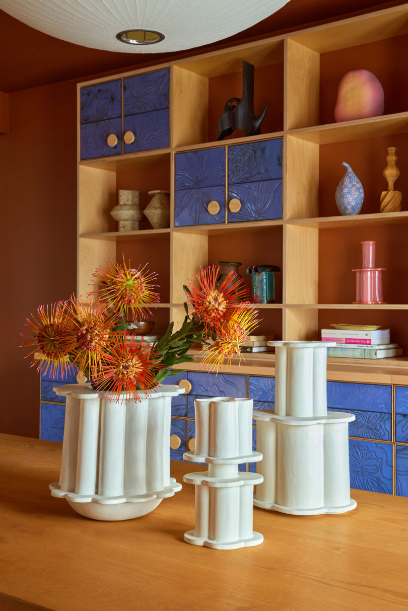three white vases resembling modern columns in front of a styled bookcase