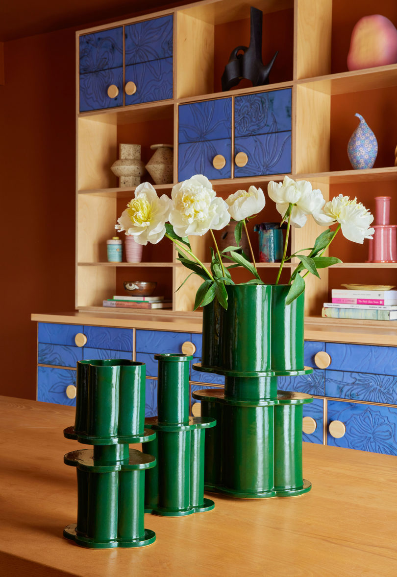 three dark green vases resembling modern columns in front of a styled bookcase