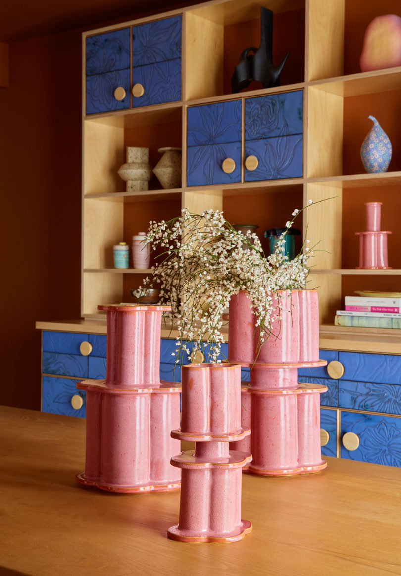three bubblegum pink vases resembling modern columns in front of a styled bookcase