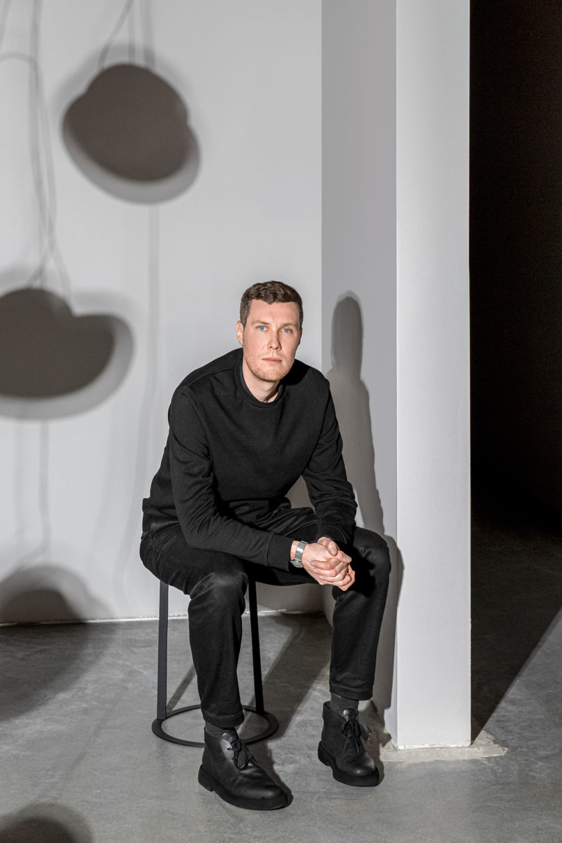 light-skinned man wearing all black clothing and sitting for a portrait