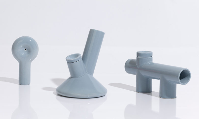 Three ceramic smoking pipes in light blue gray finish against all white shiny surface.