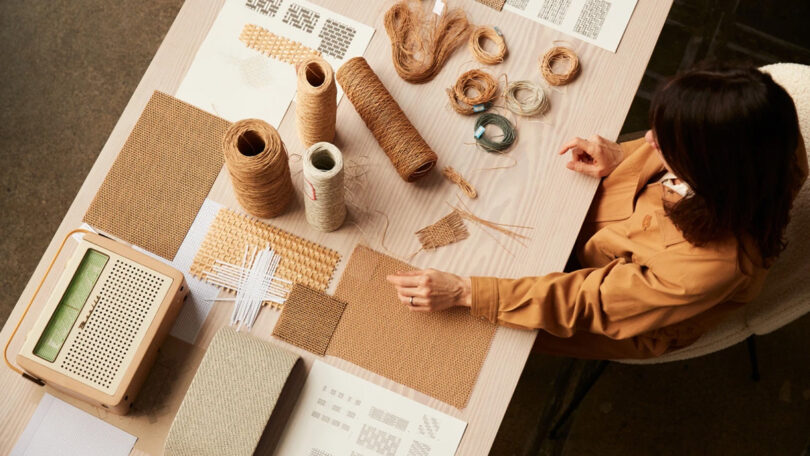 Danish architect Stine Gam seated at table reviewing natural weave materials in spools and wound up across large wooden table.