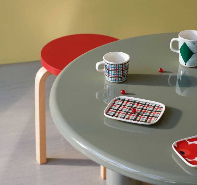 Gray round glossy table with two ceramic mugs and two small trays with red stool underneath,