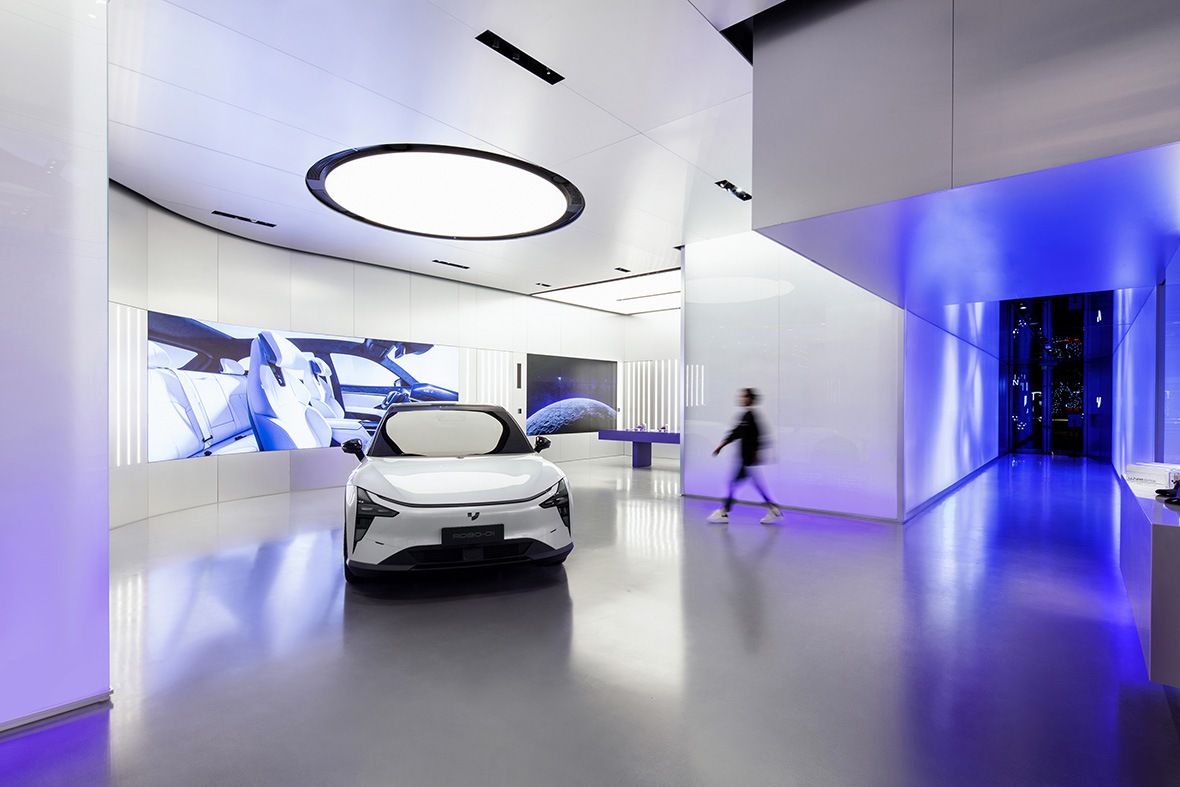 JIDU Showroom with white Robocar parked over large spotlight with person walking from purple illuminated hallway.