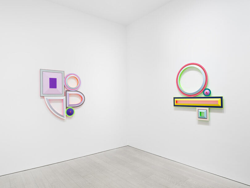 white walled gallery space with two colorful, geometric sculptural paintings