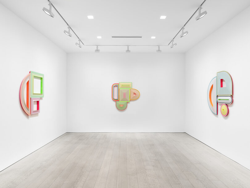 white walled gallery space with three colorful, geometric sculptural paintings