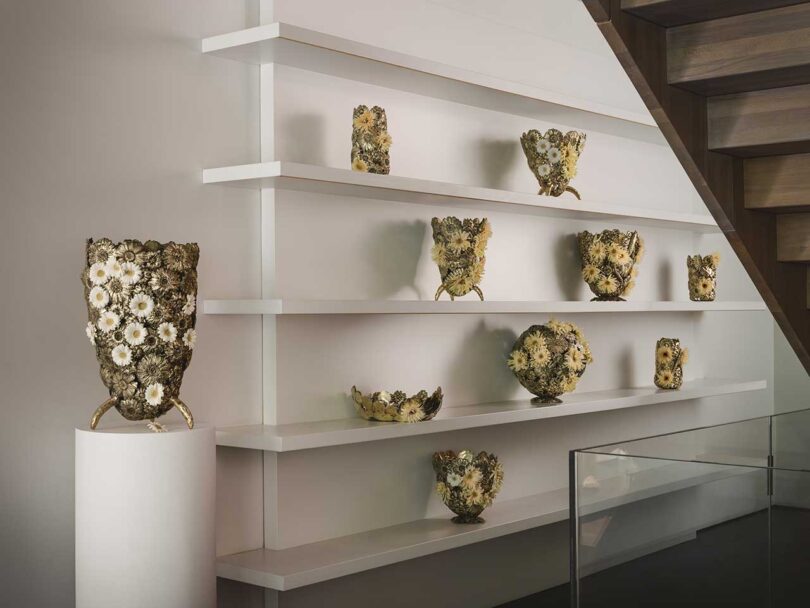 angled view of white shelves holding sculptural brass and flower vases and objects