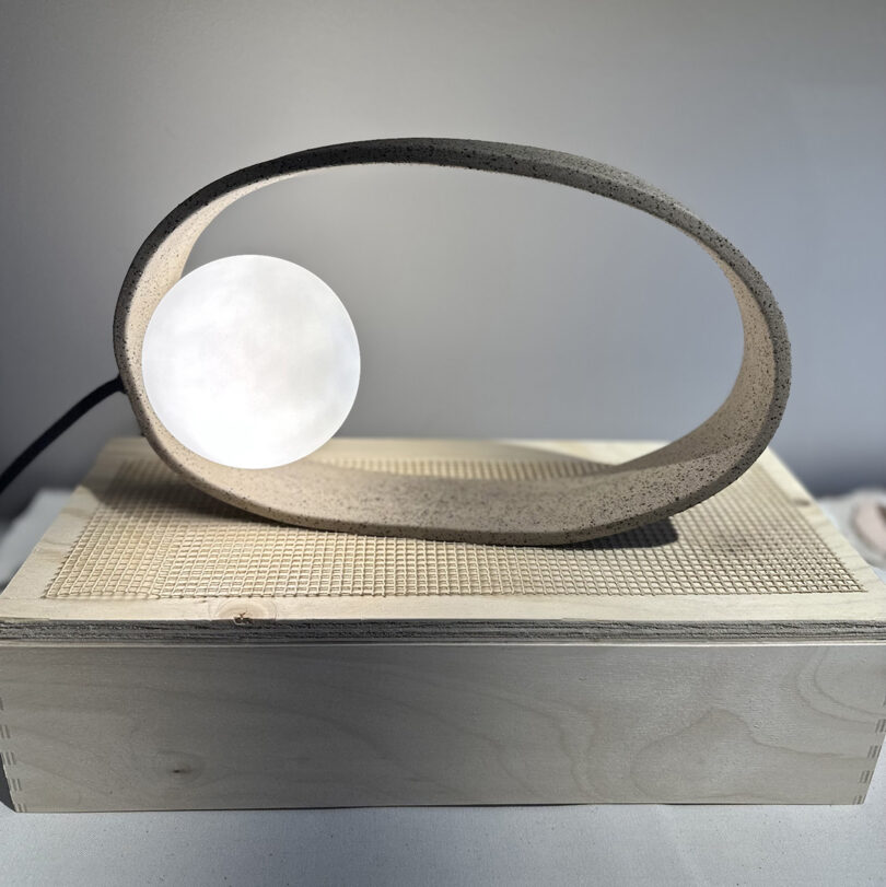 Circular folded paper table lamp on wooden pedestal with mesh rectangle on the top lid of the box.