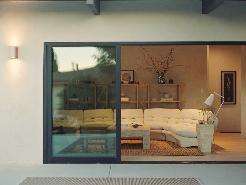 exterior shot looking into modern living room through sliding glass doors with l-shaped white sofa